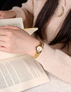 Montre bracelet dorée élégante avec petit cadran blanc portée par une femme lisant