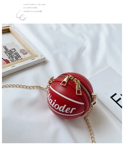 Detail shot of red basketball-shaped mini crossbody bag with gold chain on white fabric