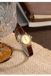 Macro shot of vintage gold oval watch with brown leather strap on rustic textured linen
