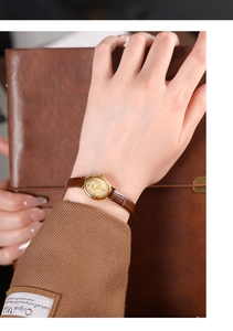 Close-up of vintage gold quartz watch with small oval dial and brown leather strap on wrist