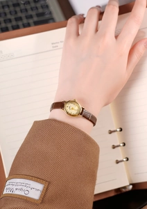 Close-up of a vintage-style gold ladies quartz watch with a brown leather strap worn on wrist
