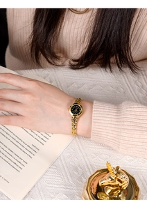 Montre chaîne dorée pour femme avec cadran noir minimaliste sur fond de livre ouvert chic