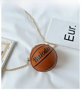 Detail of a basketball shaped kids cross body bag with gold chain on white fabric