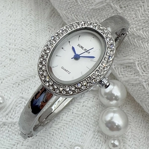 Détail d'une montre bracelet argentée avec lunette en cristal et cadran ovale blanc