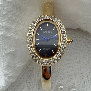 Vue macro d'une montre bracelet à quartz ovale plaquée or avec aiguilles bleues et strass