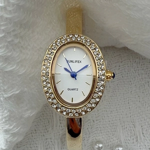 Détail d'une montre bracelet ovale dorée avec lunette sertie de diamants et couronne bleue