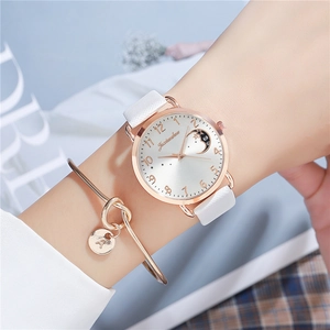 Close-up of white leather watch with star moon dial and matching gold charm bracelet