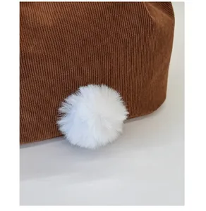 Detail of cute white plush pompom on brown corduroy backpack fabric with soft texture