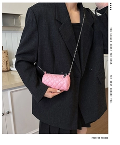 Pink quilted cylinder crossbody bag with silver chain strap worn over an oversized suit