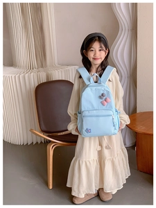 Detail of light blue school backpack featuring cute checkered bow and flower decorations