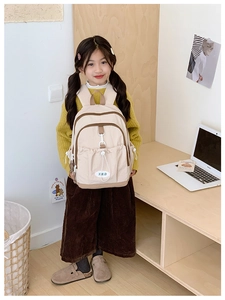 Detail view of a cream-colored minimalist school backpack worn by a young girl in a study room