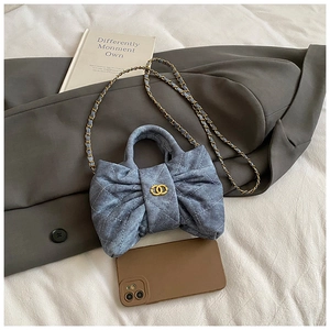 Detail of blue denim quilted handbag featuring a bow shape and gold metal chain strap