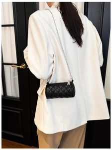 Detail of a mini black quilted barrel bag with a silver chain strap shown on a model