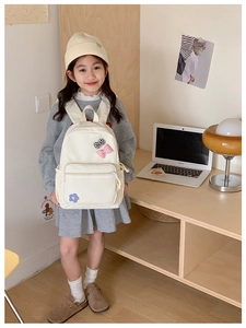 Detail of cute cream school backpack with floral bow on a young girl model at a desk