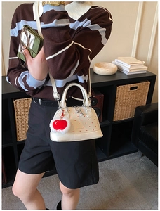 Detail of white shell handbag with red polka dots and decorative cherry plush pendant