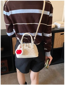 Detailansicht der weißen Muschel-Handtasche mit roten Punkten und Herz-Plüsch-Anhänger