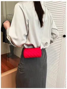 Detail of red quilted mini cylinder bag with silver chain strap worn by a child