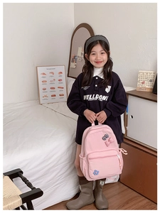 Girl holding pink school backpack with plaid bows and flower charms in a cozy bedroom