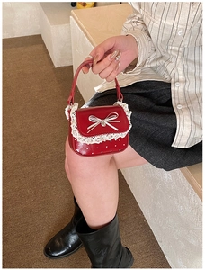 Detail of red girl's handbag featuring white lace edges and a delicate bow decoration