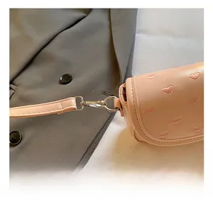 Détail du fermoir mousqueton en métal argenté sur un sac bandoulière rose brodé de cœurs