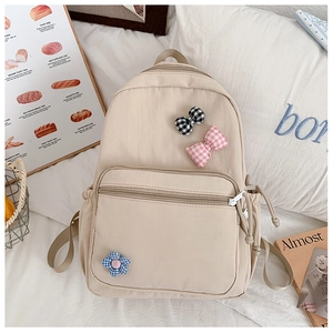 Detail view of a beige school backpack with checkered bow and floral patches on a cozy desk