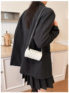 Side view of child wearing a white quilted cylinder crossbody bag with silver chain strap