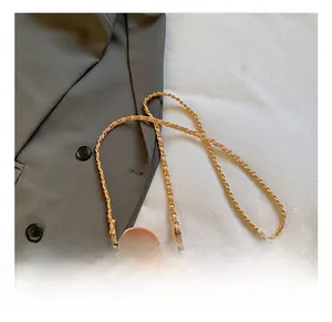 Rosa gesteppte Mini-Rundtasche mit goldener Kette und Griff neben Kleidung präsentiert