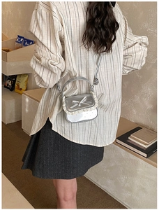 Detail of silver girls crossbody bag with lace trim and bow on striped shirt background
