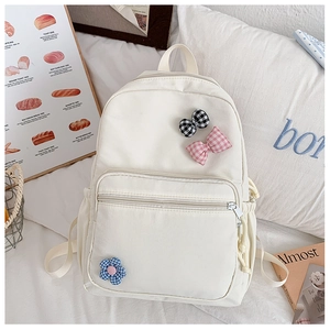 Detail of cream canvas backpack featuring decorative gingham bow and flower pins