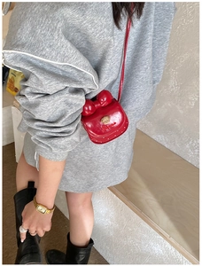 Gros plan du mini sac rouge à nœud avec ours doré porté sur un sweat-shirt gris oversize