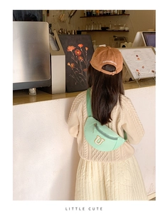 Détail d'un sac banane enfant vert menthe avec broderie lettre U dans un décor de café