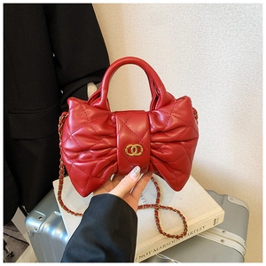 Detail of red quilted faux leather handbag featuring a bow design and gold chain strap
