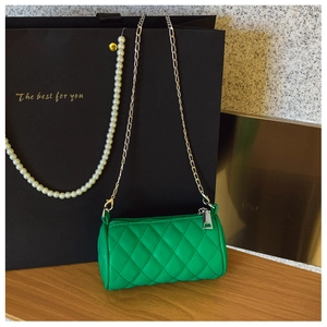 Detail of green quilted cylinder bag with metal chain strap on dark wood surface
