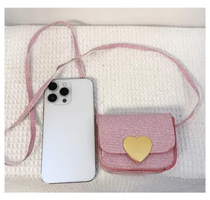 Détail du mini sac rose pailleté avec boucle cœur dorée comparé à la taille d'un téléphone