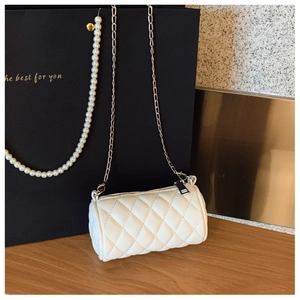 Detail of white quilted mini cylinder bag with silver metal chain on wooden desk