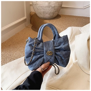 Close-up of quilted blue denim bow-shaped girls handbag with gold chain strap detail