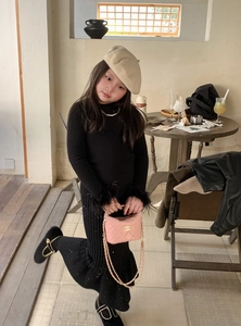 Détail d'un enfant portant une robe noire en tricot et un sac rose à chaîne matelassé