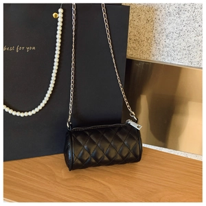 Detail of black quilted cylindrical bag with silver chain and stitched rhombus pattern