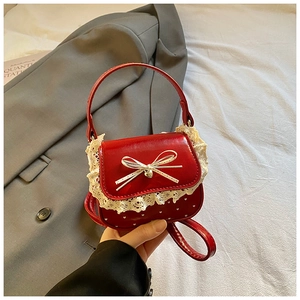 Close-up of red patent leather girl bag with lace trim, bow, and gold heart pendant