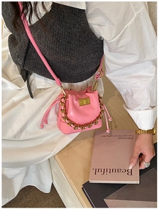 Gros plan sur le mini sac seau matelassé rose avec chaîne dorée porté par un mannequin