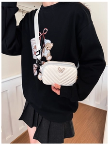 Close-up of a white quilted chest bag with a golden butterfly charm worn by a child