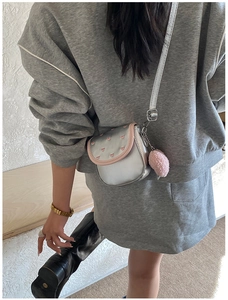 Détail du sac à bandoulière argenté avec motifs de cœurs roses et pompon en peluche