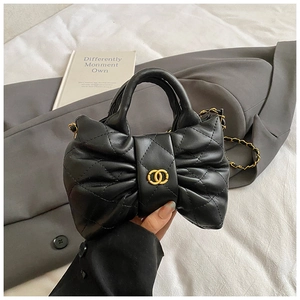 Detail of black quilted leather bag featuring bow shape and gold metal logo closure