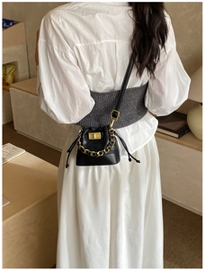 Détail d'un mini sac seau noir avec cordon et boucle dorée porté sur une robe blanche