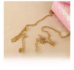 Detail shot of pink woven texture crossbody bag featuring a heavy gold metal chain strap