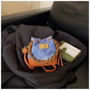 Détail du mini sac seau montrant le denim matelassé bleu, le cuir brun et la chaîne