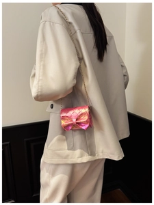 Pink holographic mini crossbody bag with bow and gold chain strap on beige suit