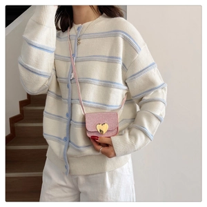 Détail du mini sac rose pailleté avec boucle cœur dorée sur un cardigan à rayures