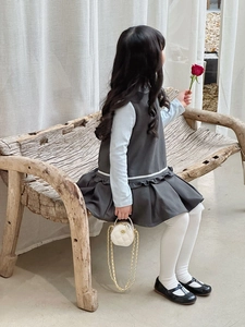 Kleinkind-Mädchen trägt graues Steppkleid und hält weiße runde Mini-Ketten-Umhängetasche