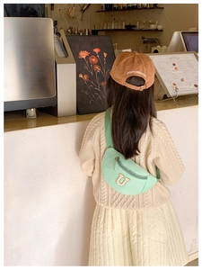 Détail du sac banane enfant en nylon vert menthe avec écusson U jaune dans un café